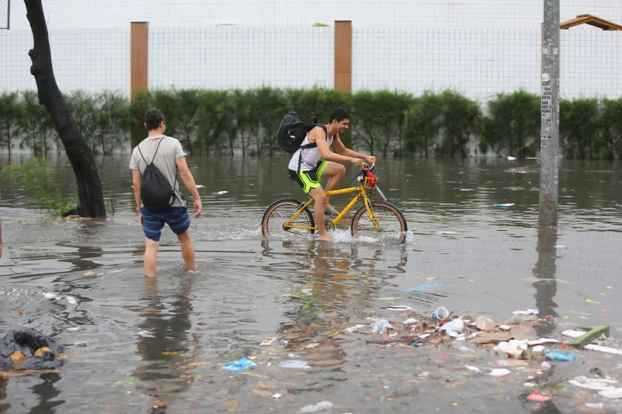 Pedestre e ciclista atravessam via alagada em Fortaleza em maio de 2021
