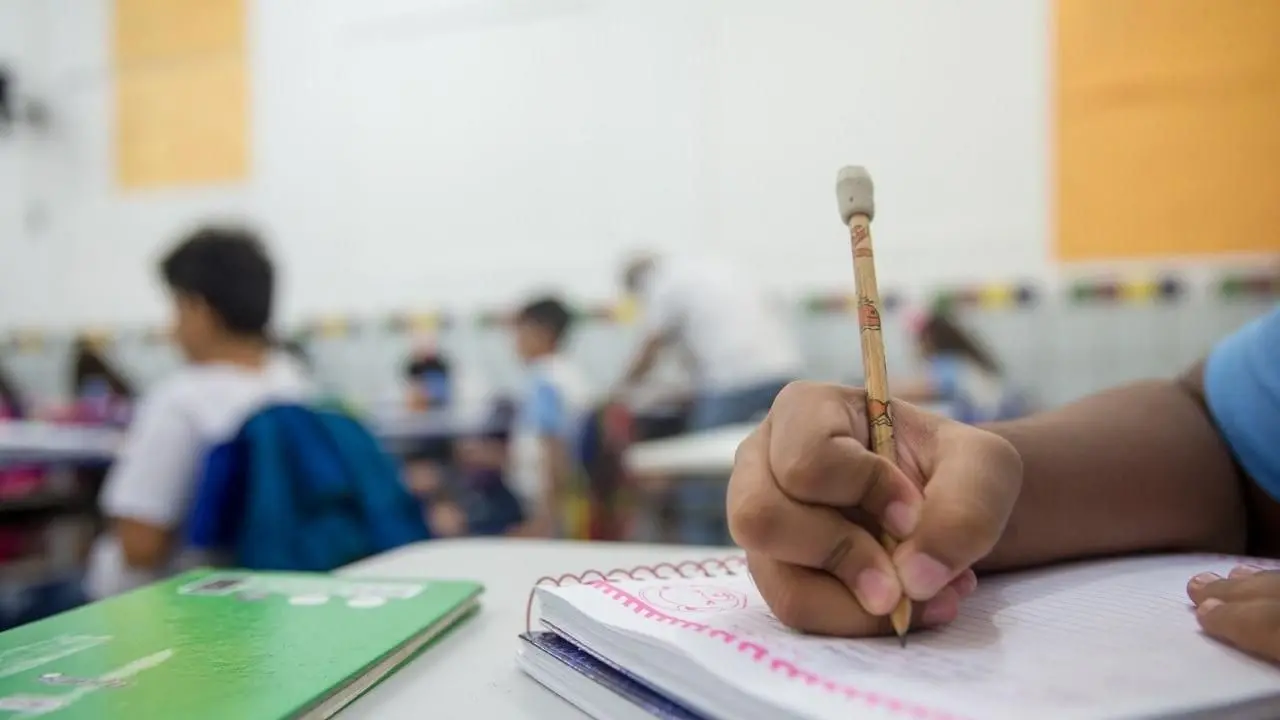 mão de criança segurando lápis e escrevendo em caderno