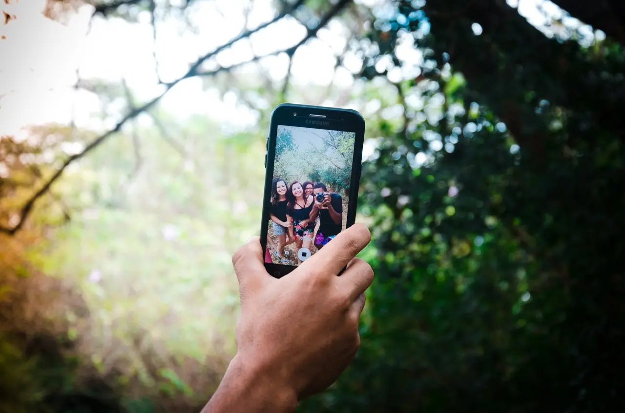 mão segurando celular com foto de amigos