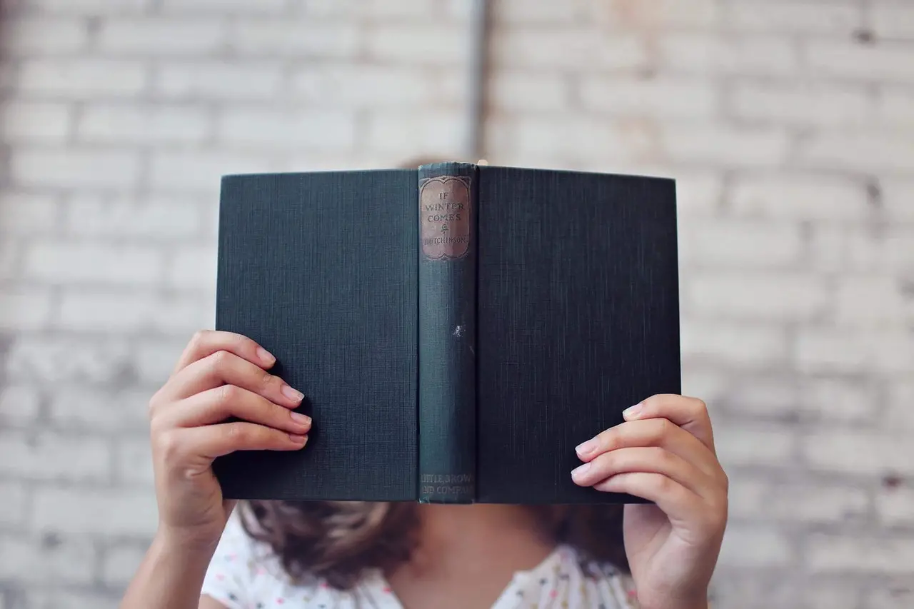 Pessoa com livro na frente do rosto