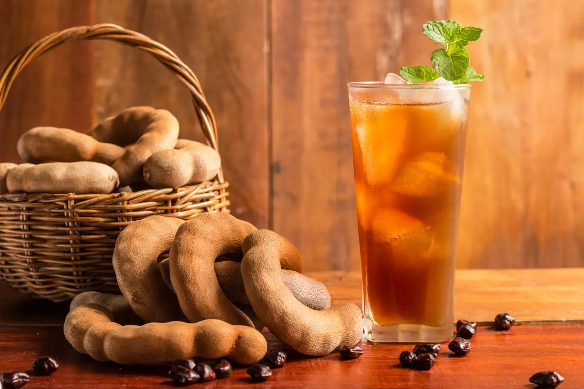 Tamarindos em uma cesta, com um copo de vidro de suco de tamarindo ao lado
