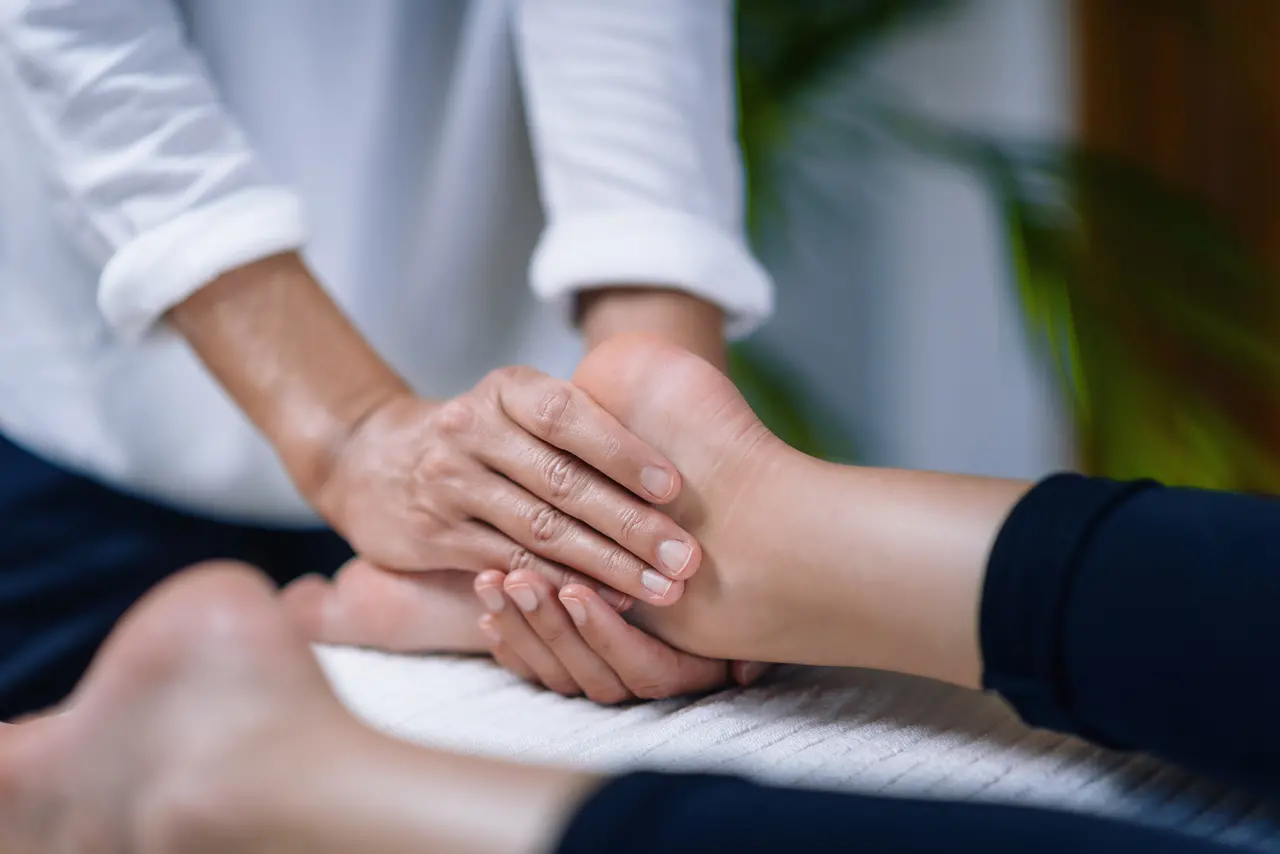 Mãos posicionadas para aplicação de Reiki no pé esquerdo da paciente