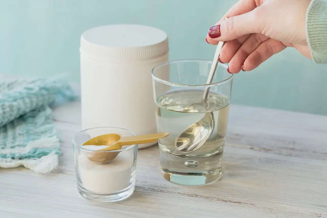Frasco com colágeno dissolvido em água e pó de proteína de colágeno em mesa de madeira branca