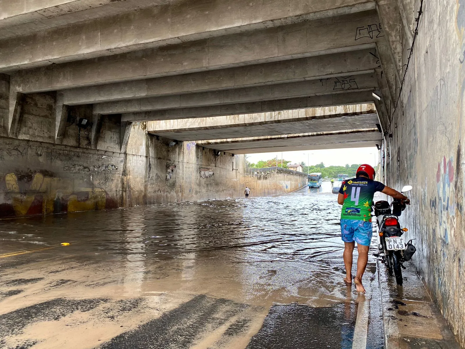 Motociclista tenta atravessar empurrando veículo.
