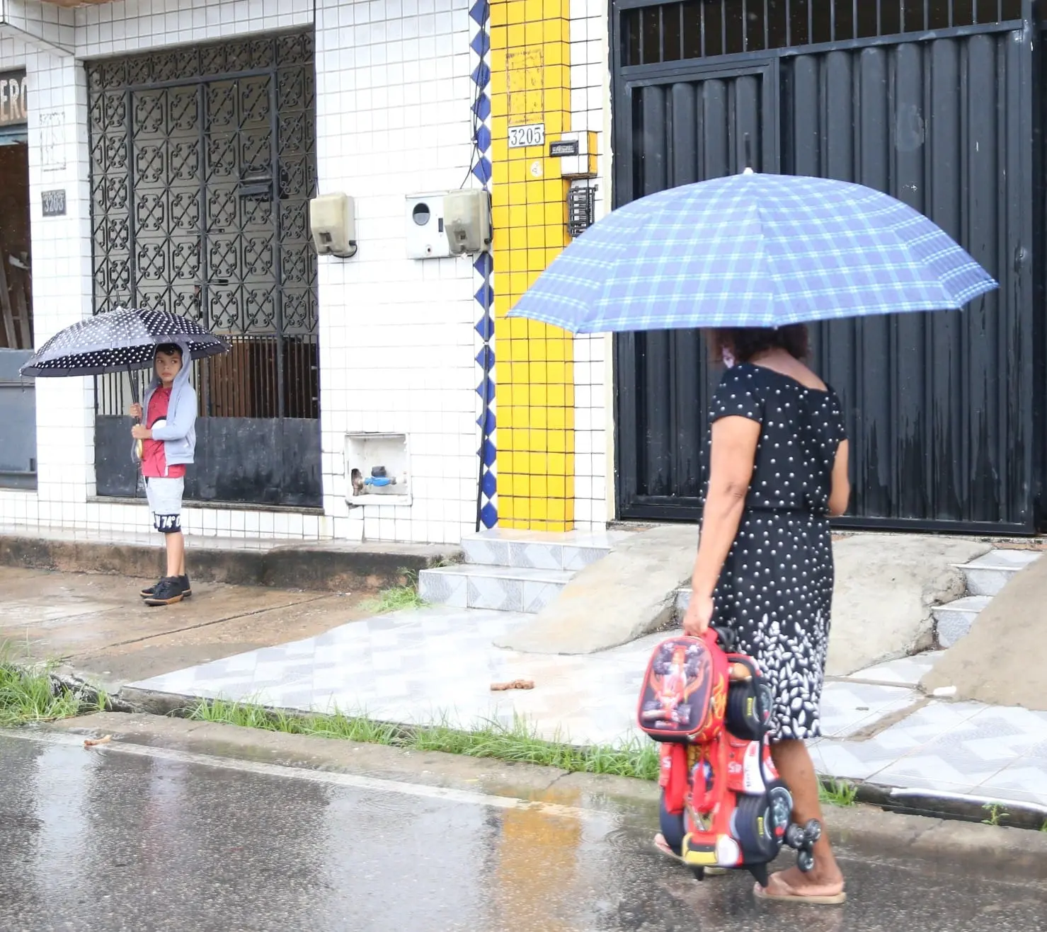 Idosa com guarda-chuva anda em direção a criança com guarda-chuva em Fortaleza