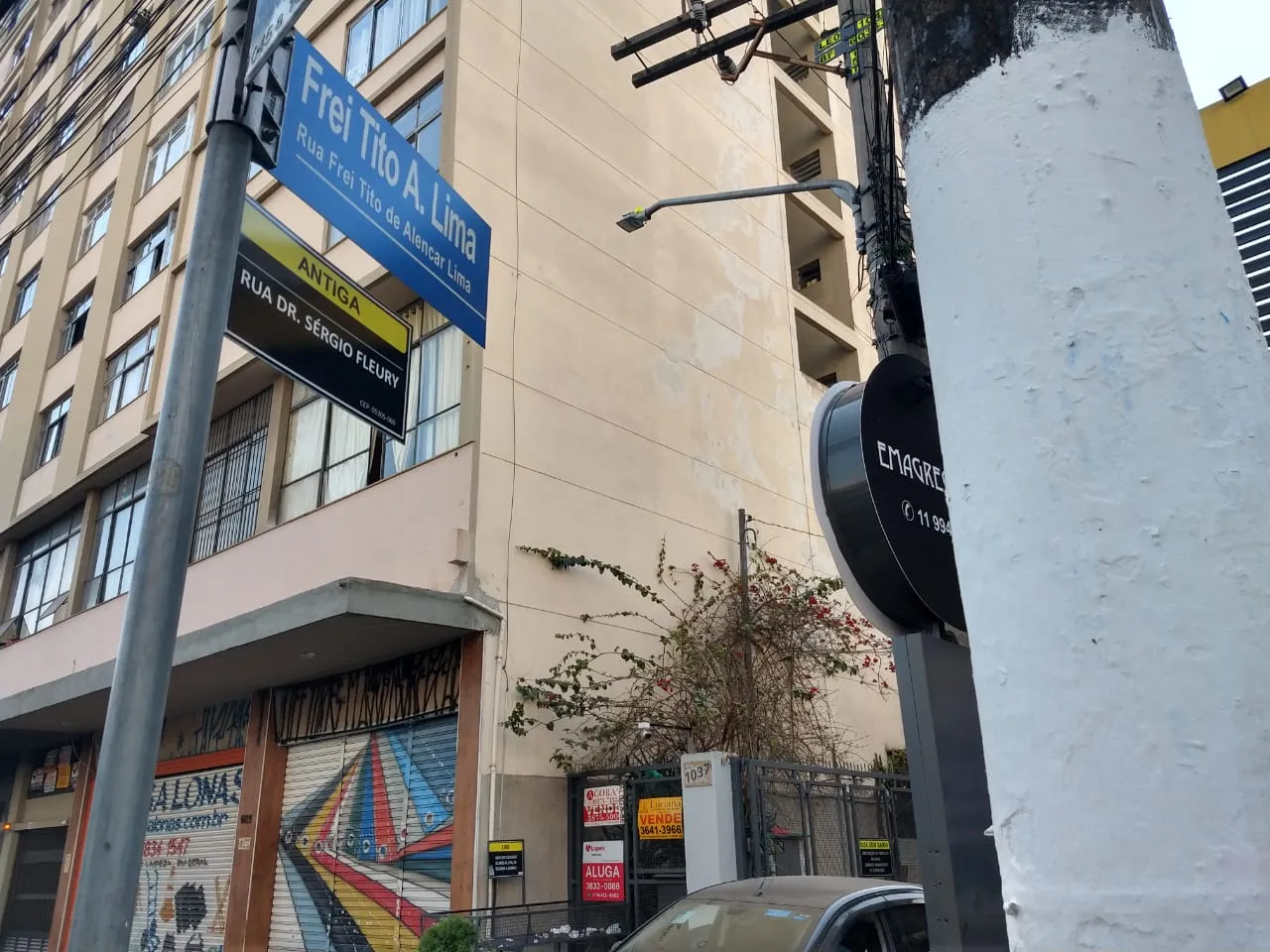 A placa oficial de localização informa: “Rua Frei Tito de Lima”. Abaixo dela há a outra placa. Essa menor, informal, feita pelos próprios moradores, diz: “Antiga Rua Dr. Sérgio Fleury”