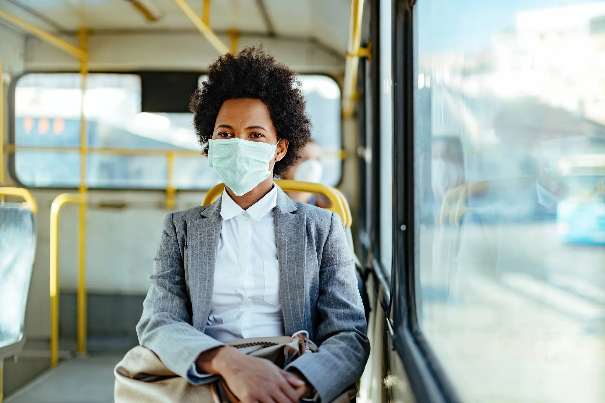 Imagem mostra mulher negra usando máscara de proteção a bordo de um ônibus público