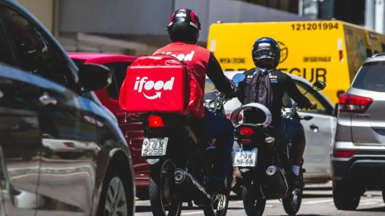 Imagem mostra entregador de aplicativo entre carros e motos de rua movimentada