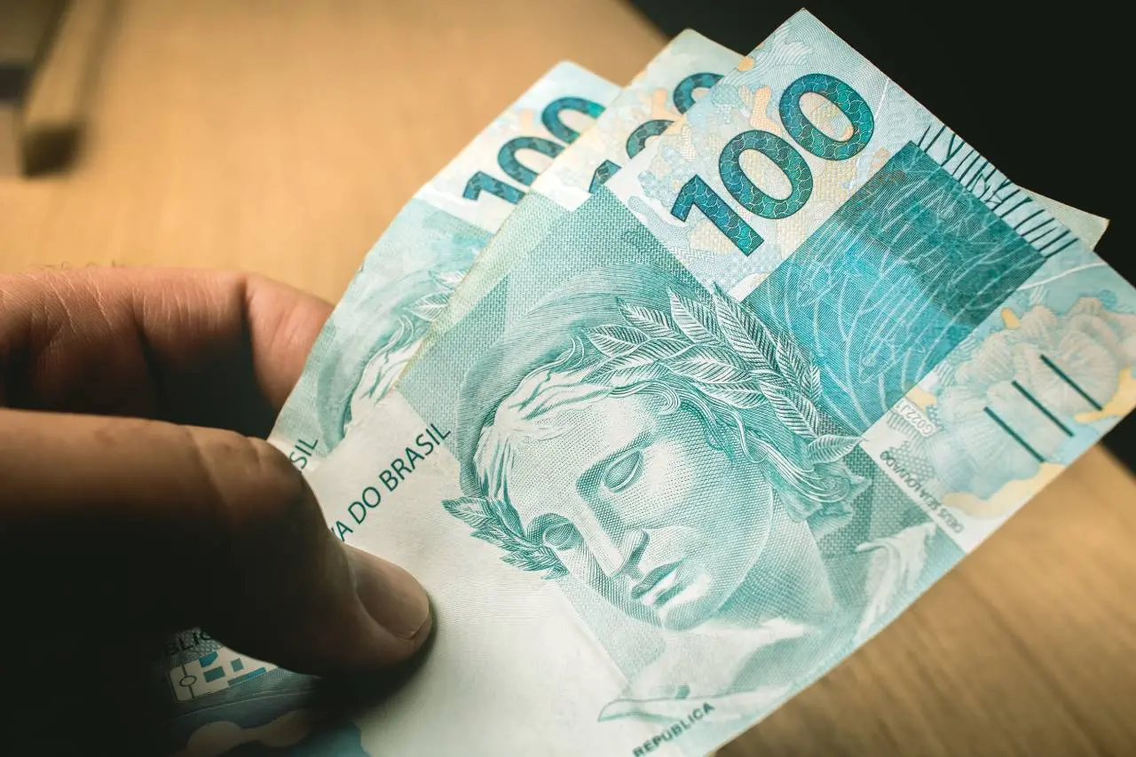 Mão segurando três notas de R$ 100