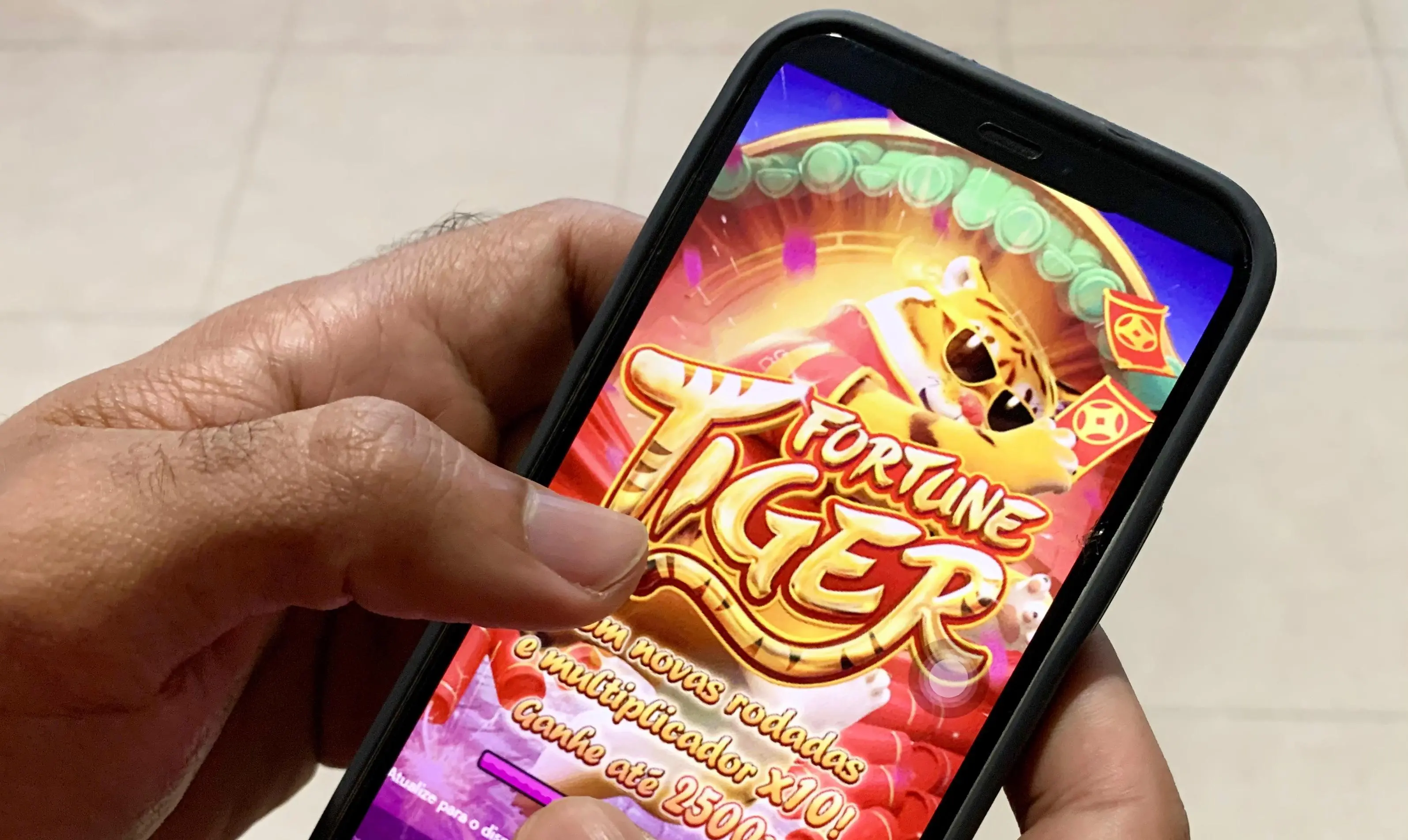 Pessoa segurando celular com jogo do tigrinho