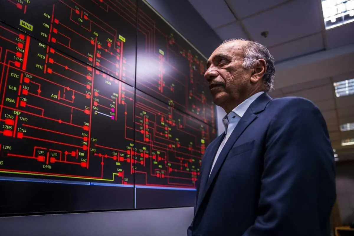 José Nunes Almeida, um homem idoso, calvo, está olhando para sistemas de energia elétrica. Ele está vestido com terno azul e camisa azul