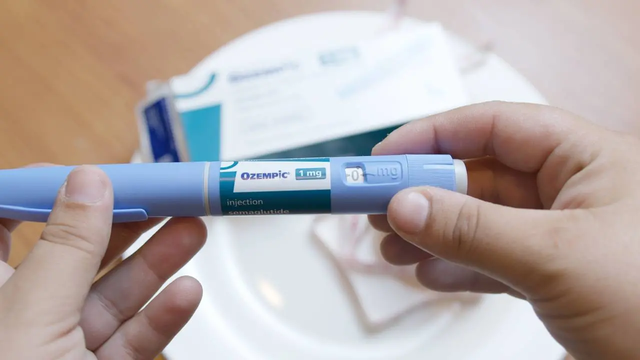 Mãos segurando uma ampola de Ozempic com a caixa do medicamento desfocada ao fundo