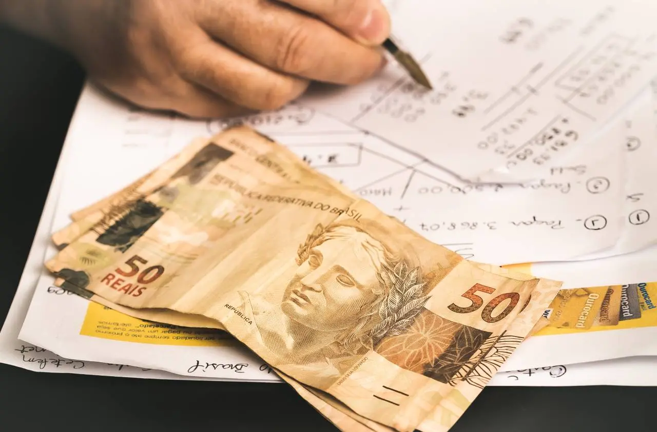 Mão fazendo cálculo com notas de R$ 50