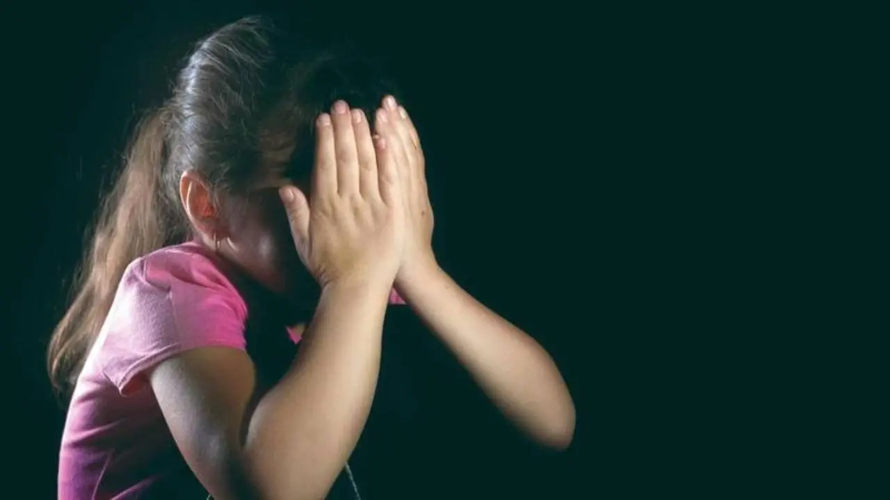 Menina escondendo o rosto com as mãos em imagem com fundo preto