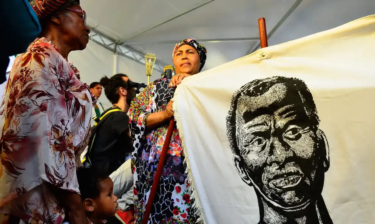Mulheres negras segurando um tecido com a imagem de Zumbi dos Palmares