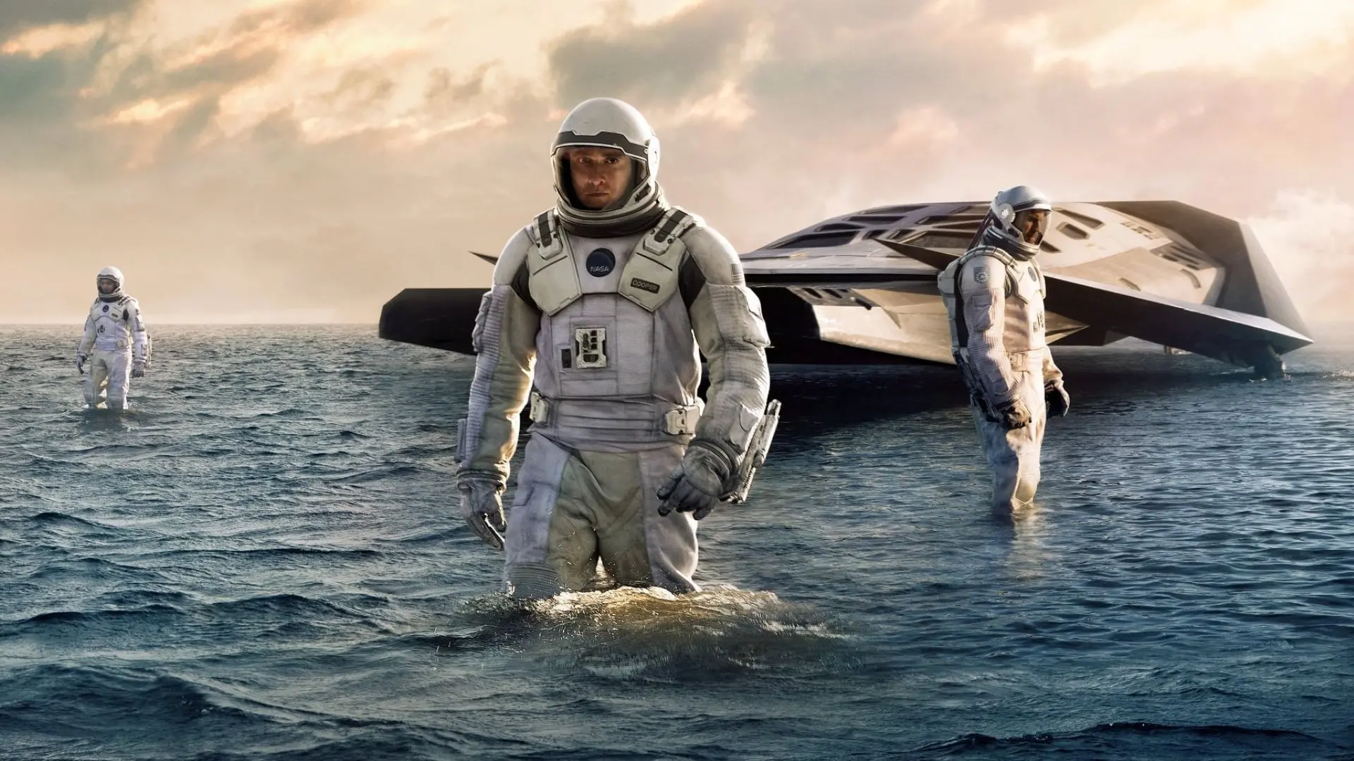 Imagem promocional do filme Interestelar mostrando astronautas, uma nave e um planeta com água