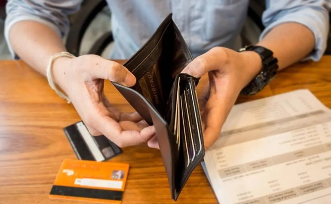 Mão abre carteira vazia em cima de mesa com cartões de crédito