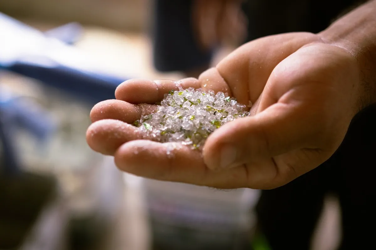 O vidro é produzido a partir da fusão de diversos materiais, como a areia. No processo realizado pela cooperativa, as garrafas de vidro retornam a essa forma
