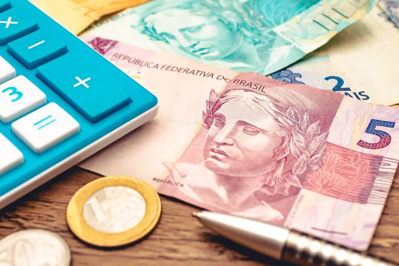 Notas e moedas de Real ao lado de calculadora