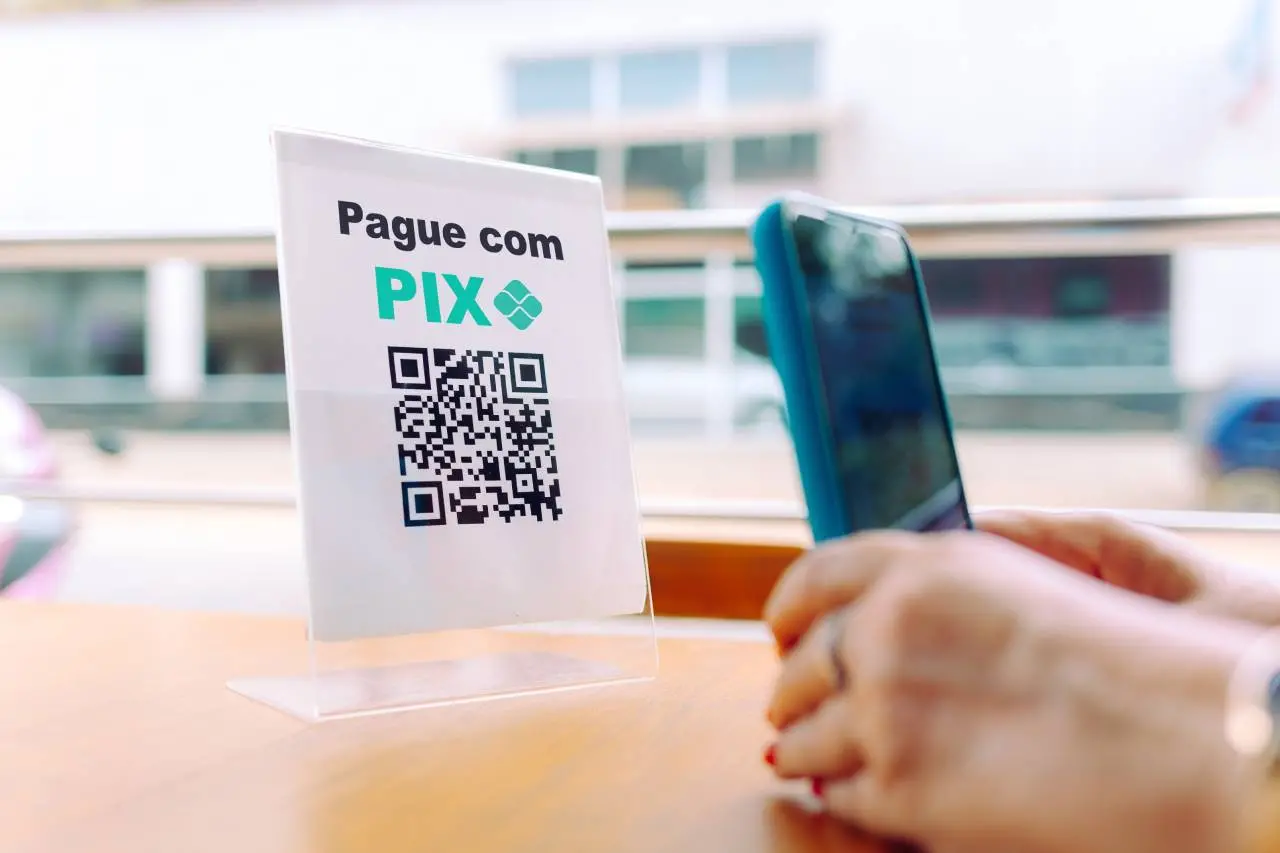 Mãos segurando celular para escanear Código QR sobre mesa