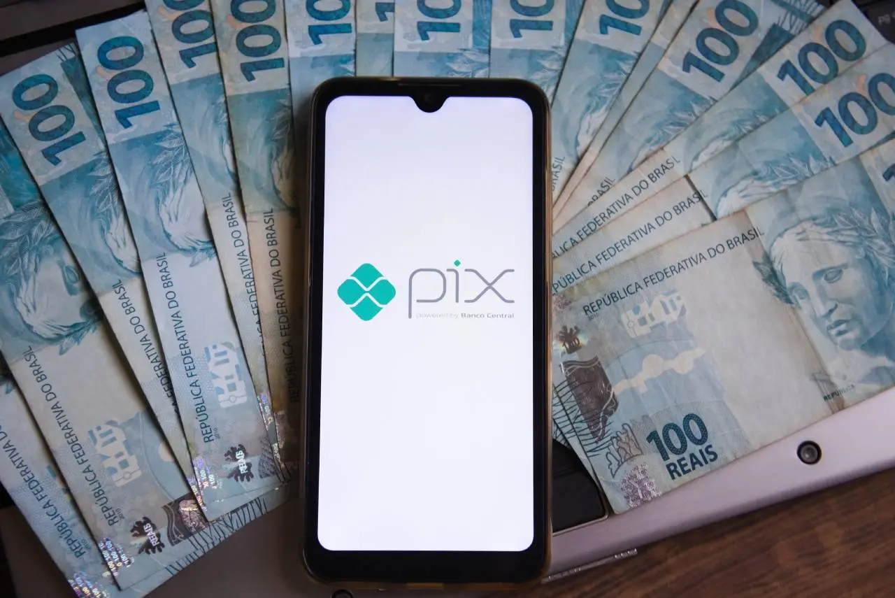 Celular mostrando logo do Pix sobre notas de R$ 100