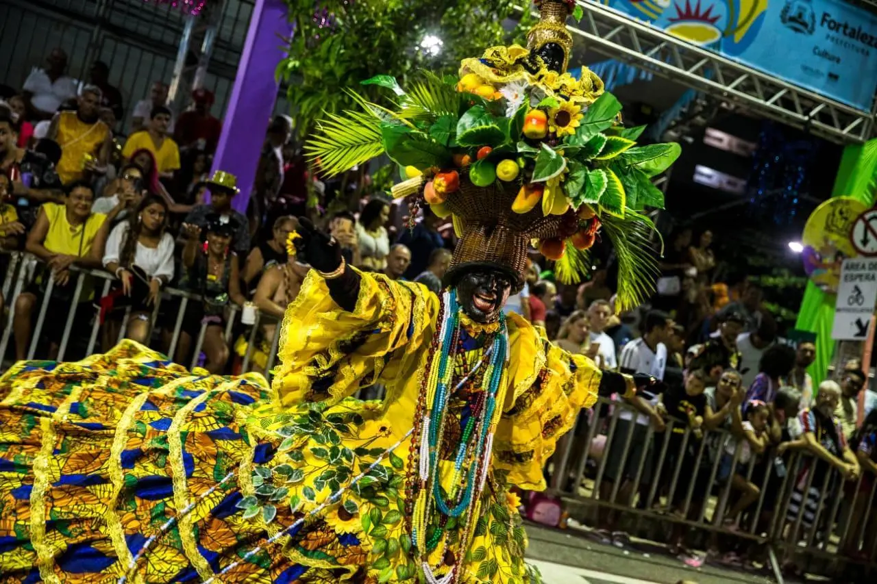 Foto de participante de um desfile de carnaval em Fortaleza, vestido com fantasia vibrante de frutas e folhagens.