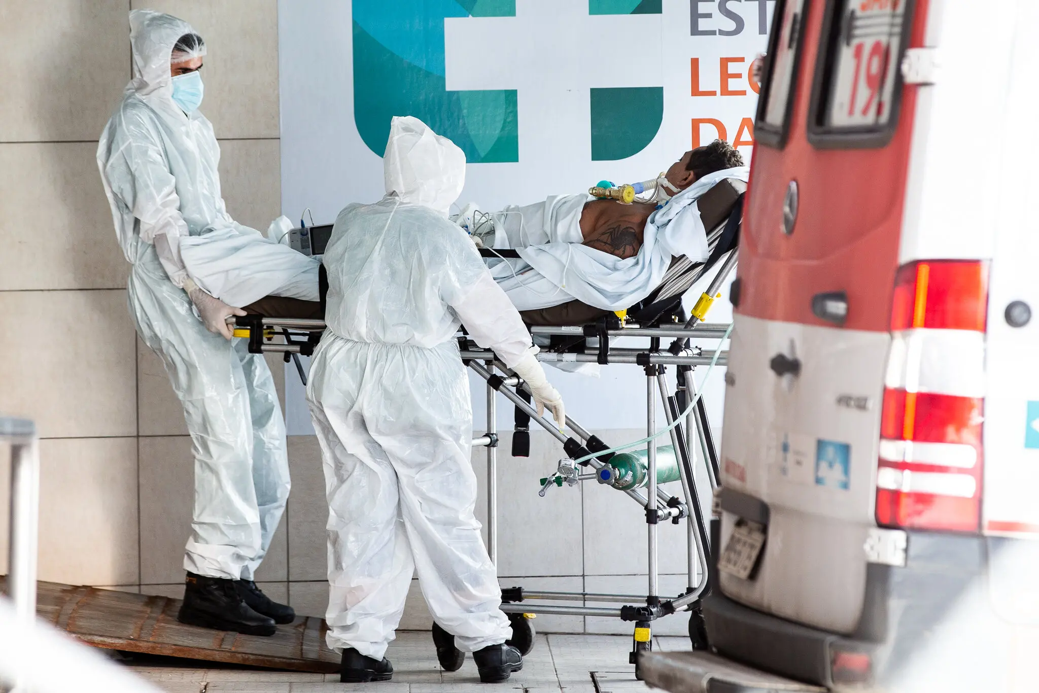 Profissionais da saúde com roupa especial para evitar contágio retiram paciente de ambulância