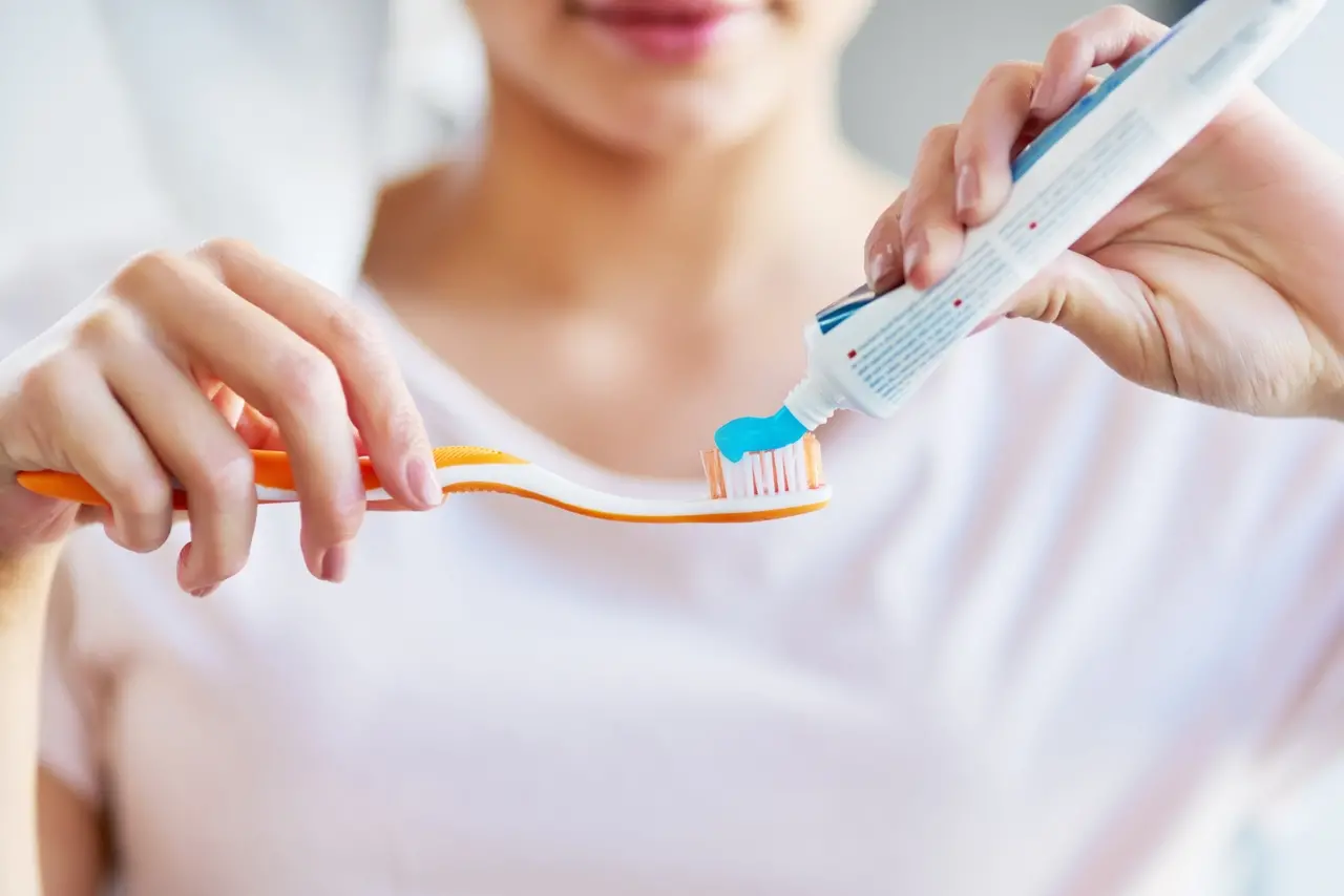 Imagem mostra close-up de uma jovem espremendo creme dental em sua escova de dentes no banheiro de casa. Creme dental: dentista explica como escolher, sintomas de alerta e substâncias que podem causar reações adversas