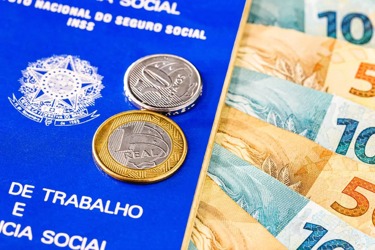 Carteira de Trabalho com notas e moedas de real indicando o empréstimo consignado para empresados pela CLT