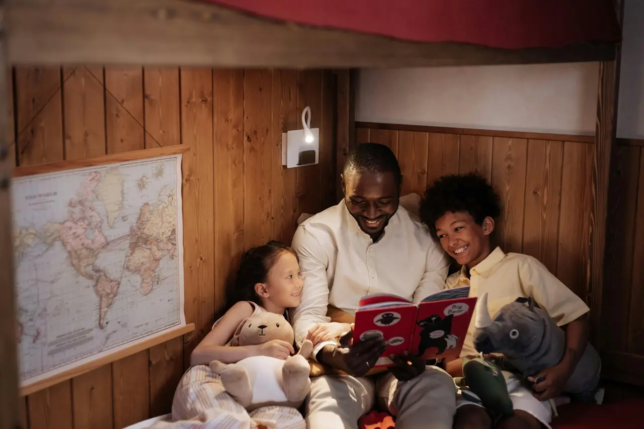 Homem adulto negro lendo um livro para uma menina e um menino, ambos negros