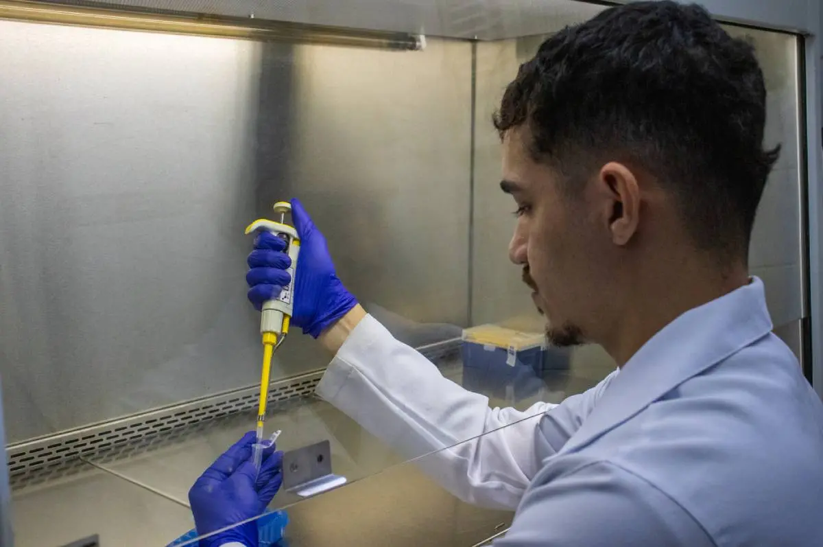 Pesquisador em laboratório. Ele usa jaleco branco e está manuseando uma seringa