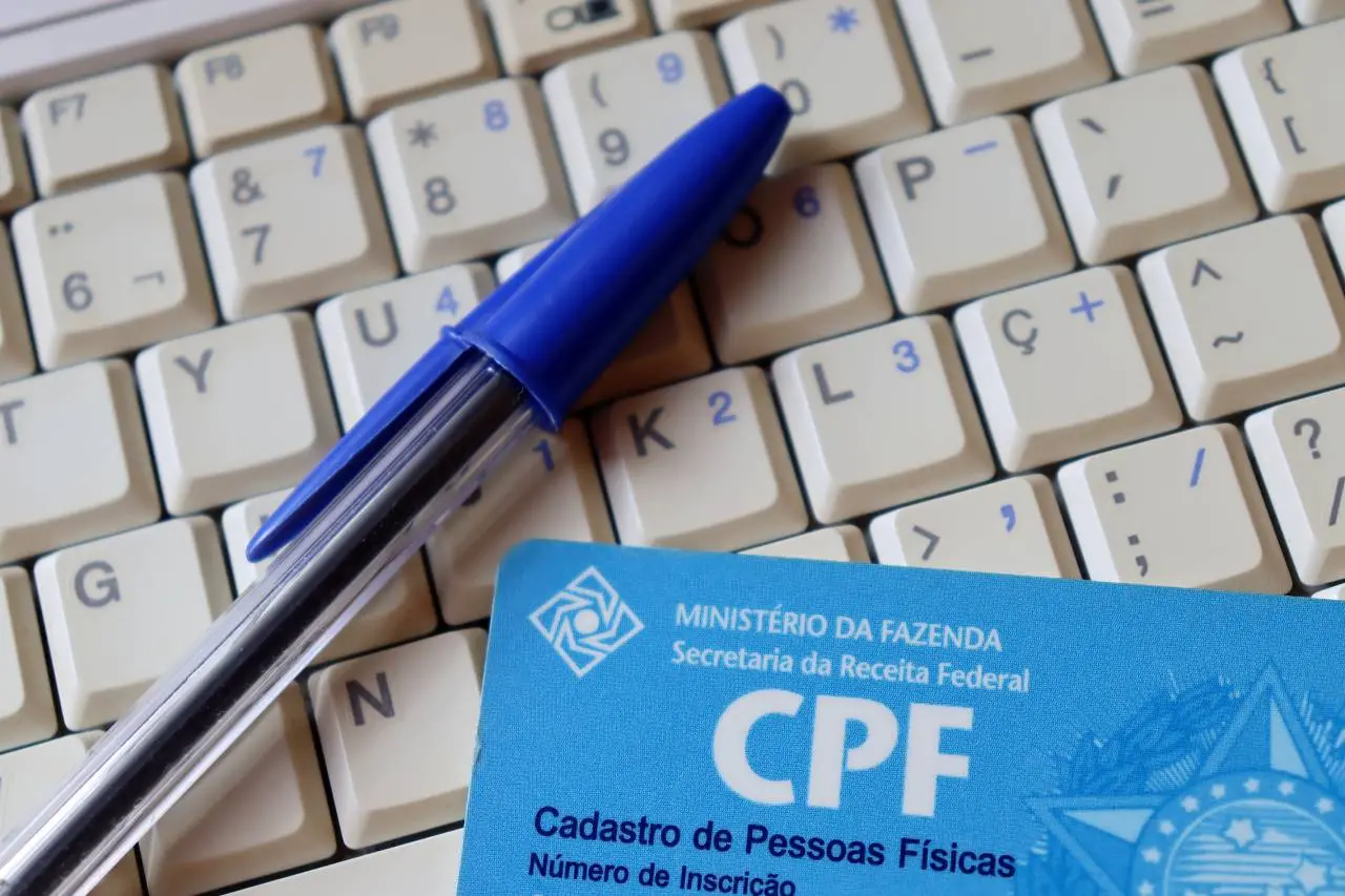 Carteira de CPF sobre teclado de computador com caneta ao lado