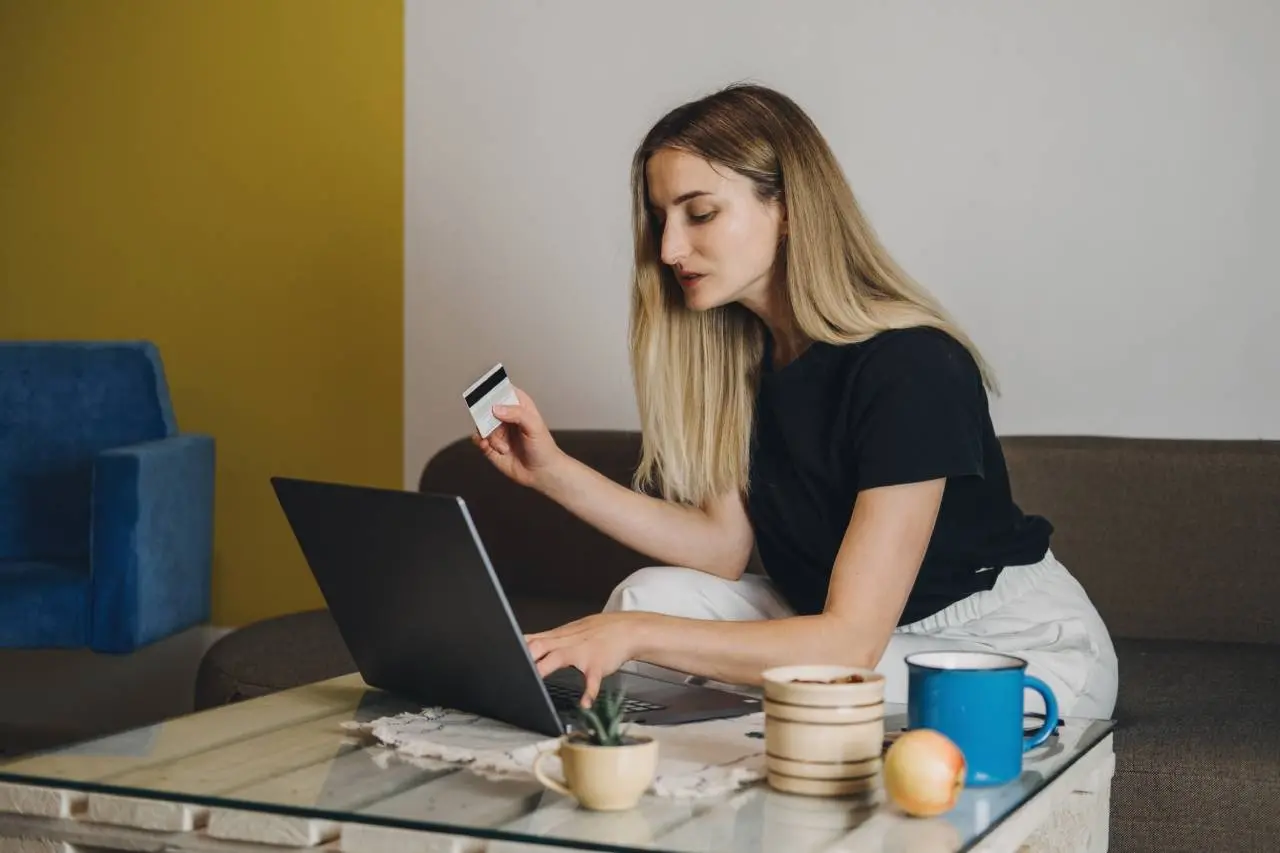 Mulher segurando cartão de crédito enquanto mexe em computador