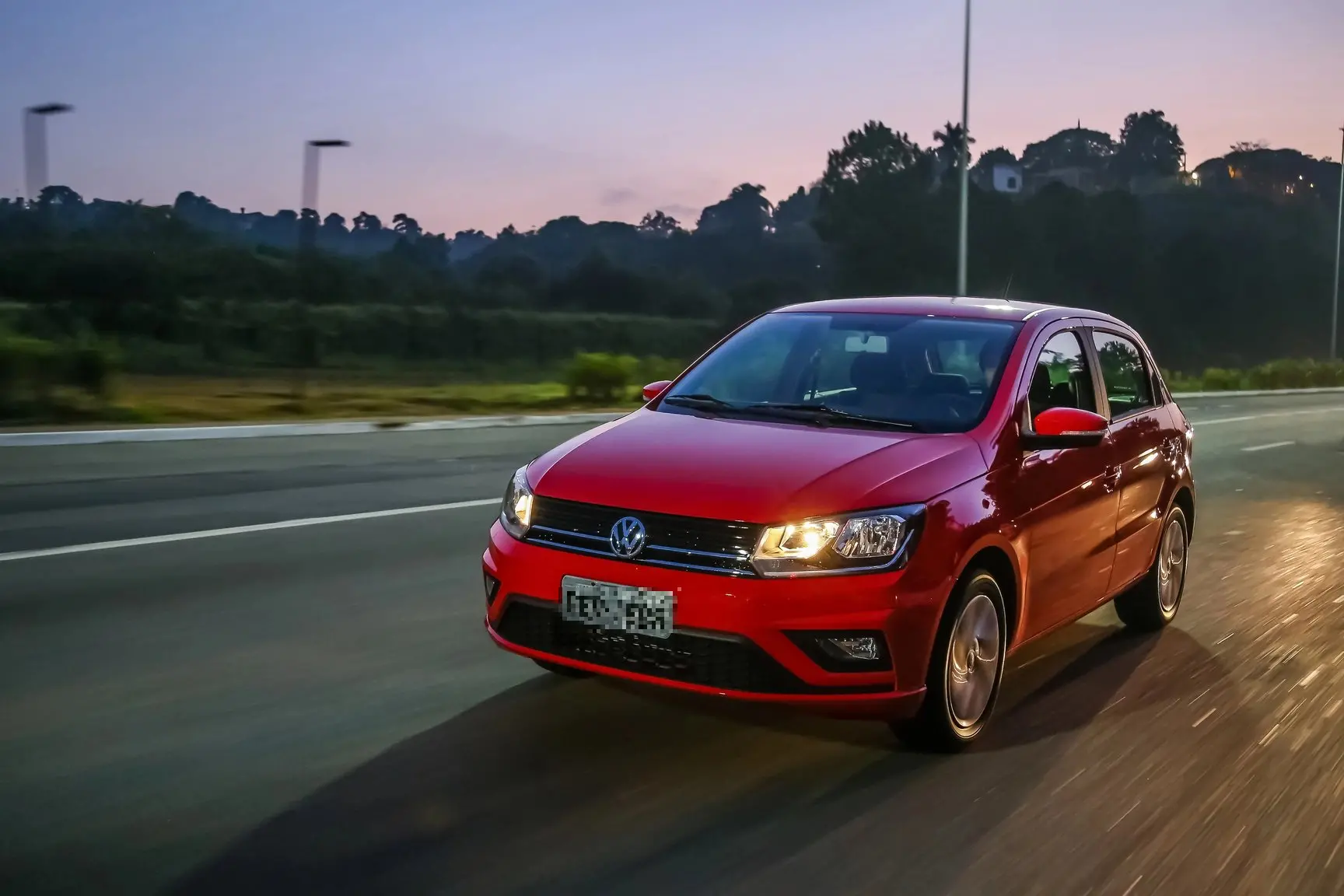 Imagem mostra carro Gol na cor vermelha com os faróis acesos, em uma estrada