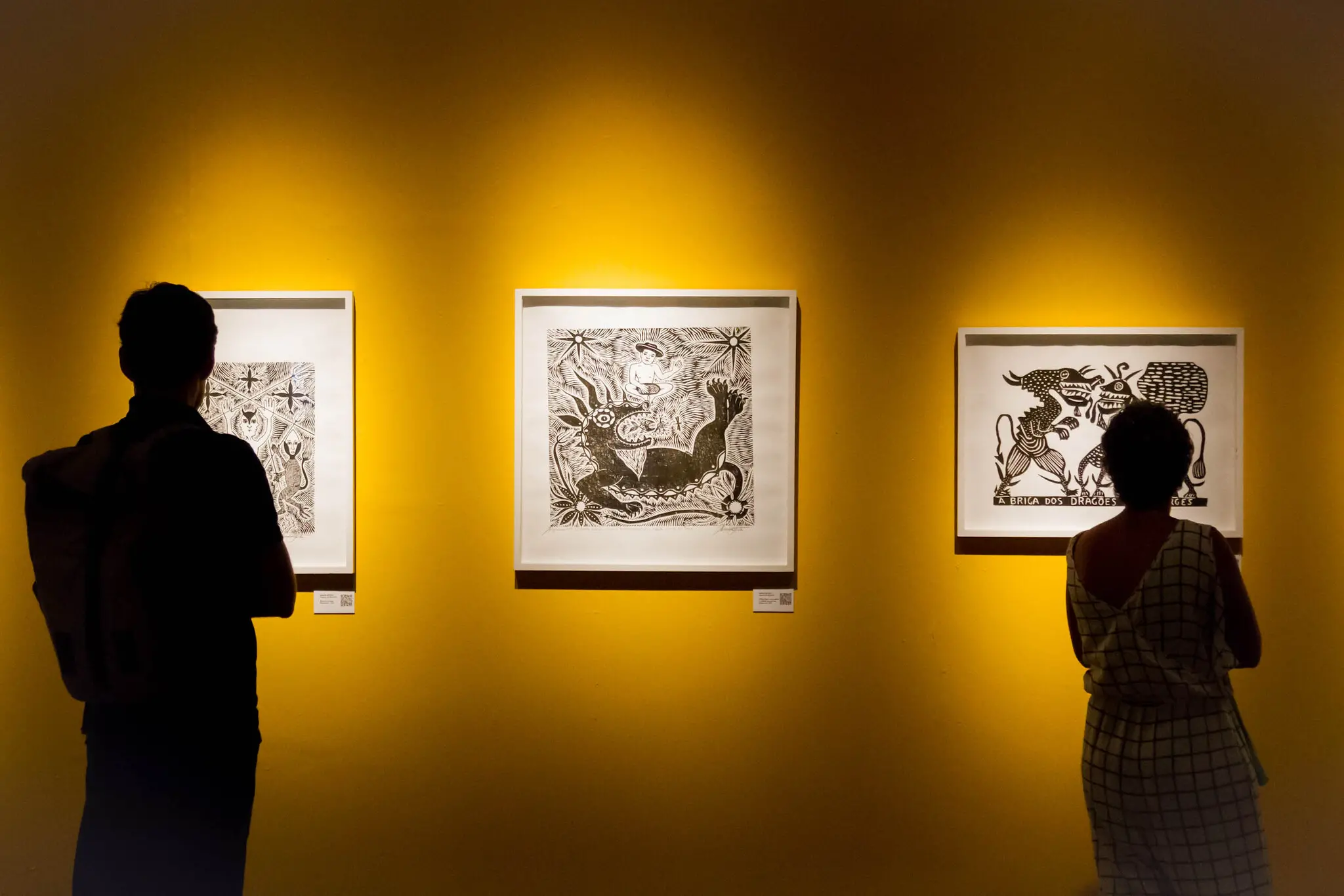 Silhueta de um homem e uma mulher observando obras de xilogravura