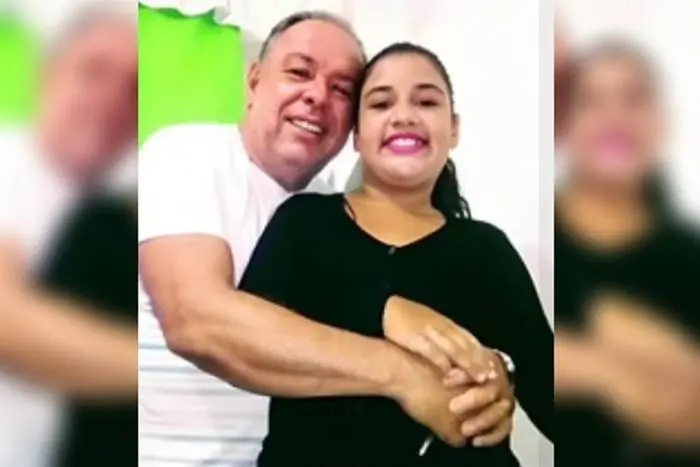 Na imagem, pai e filha aparecem abraçados. Ele é um homem branco e grisalho, enquanto ela é uma mulher jovem de cabelos amarrados