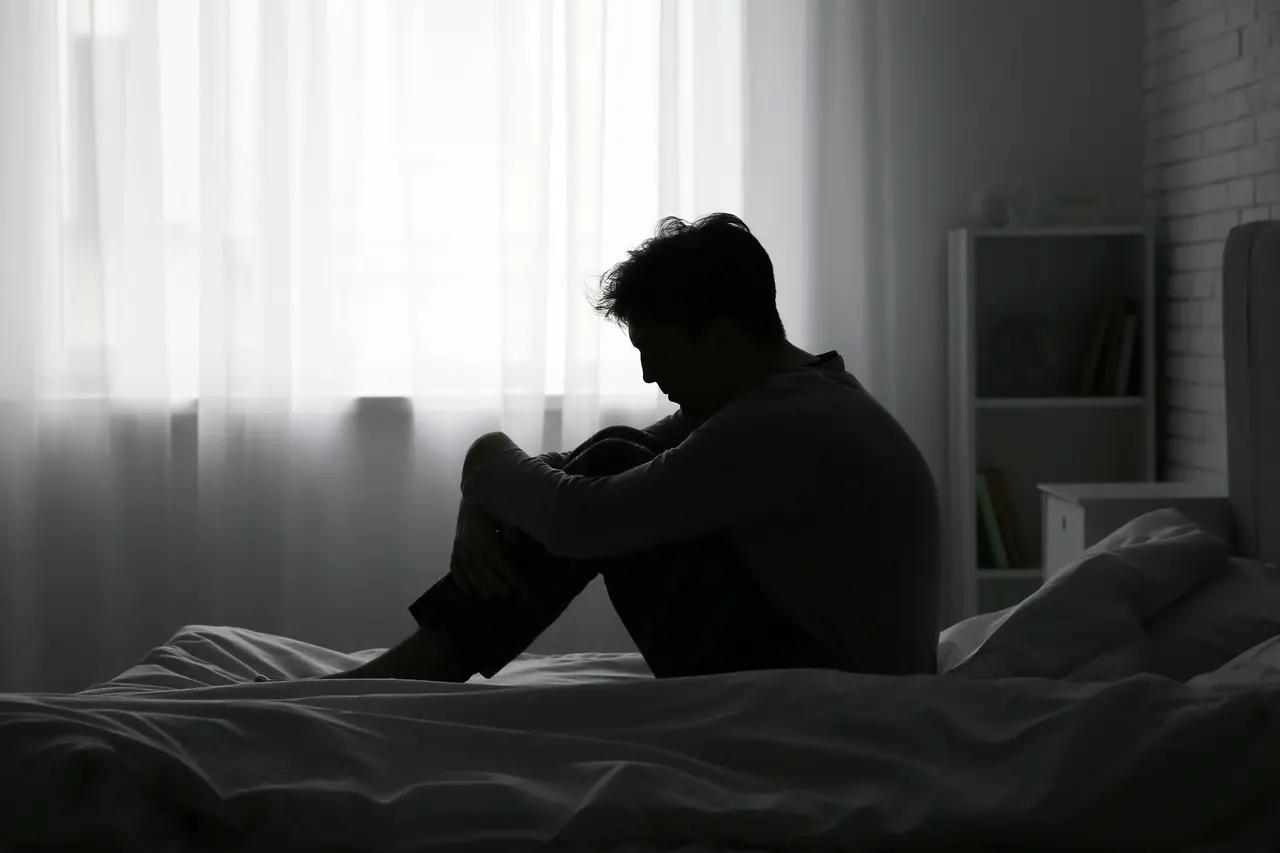 imagem de uma pessoa no escuro, sentada em uma cama,  que sugere adoecimento mental