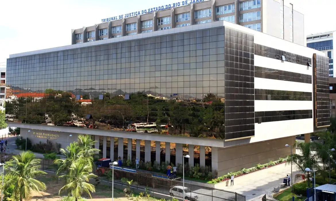 Edifício do Tribunal de Justiça do Estado do Rio de Janeiro com fachada de vidro, localizado em uma área urbana com árvores e pessoas na frente.