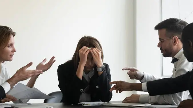 Profissionais em uma reunião apontam o dedo para uma profissional