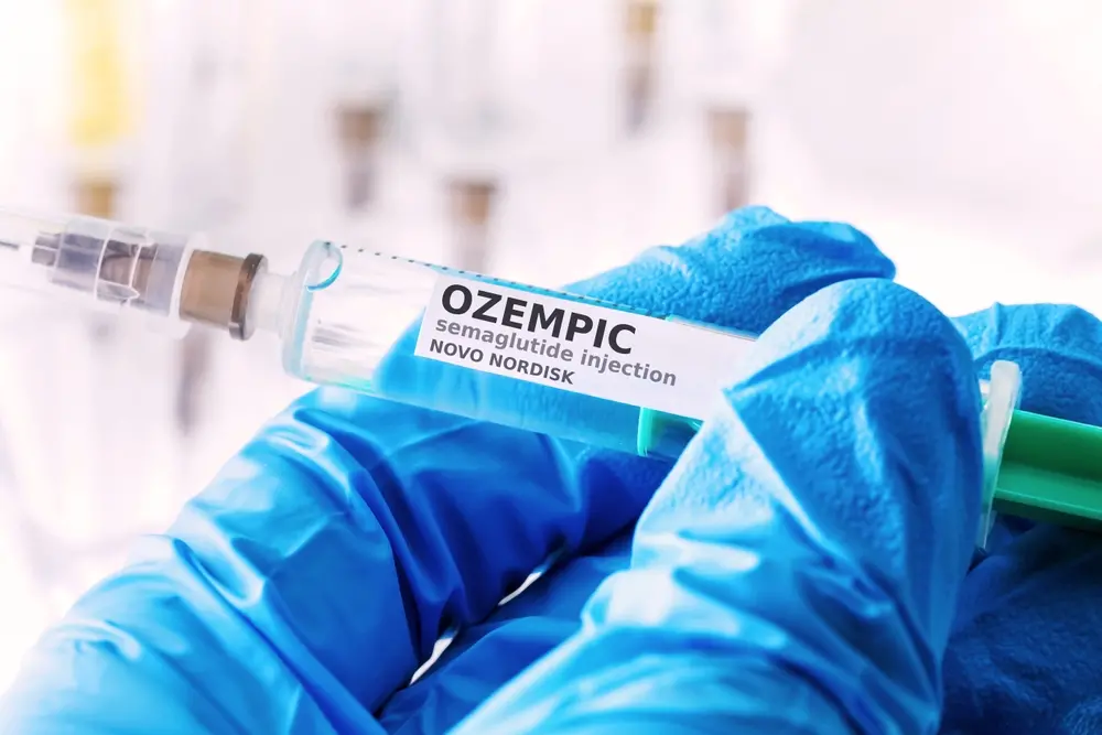 Imagem de uma pessoa com luvas azuis segurando uma seringa com um frasco de vacina Ozempic na área de saúde, destacando o uso do medicamento Ozempic para tratamento de diabetes e controle de peso.