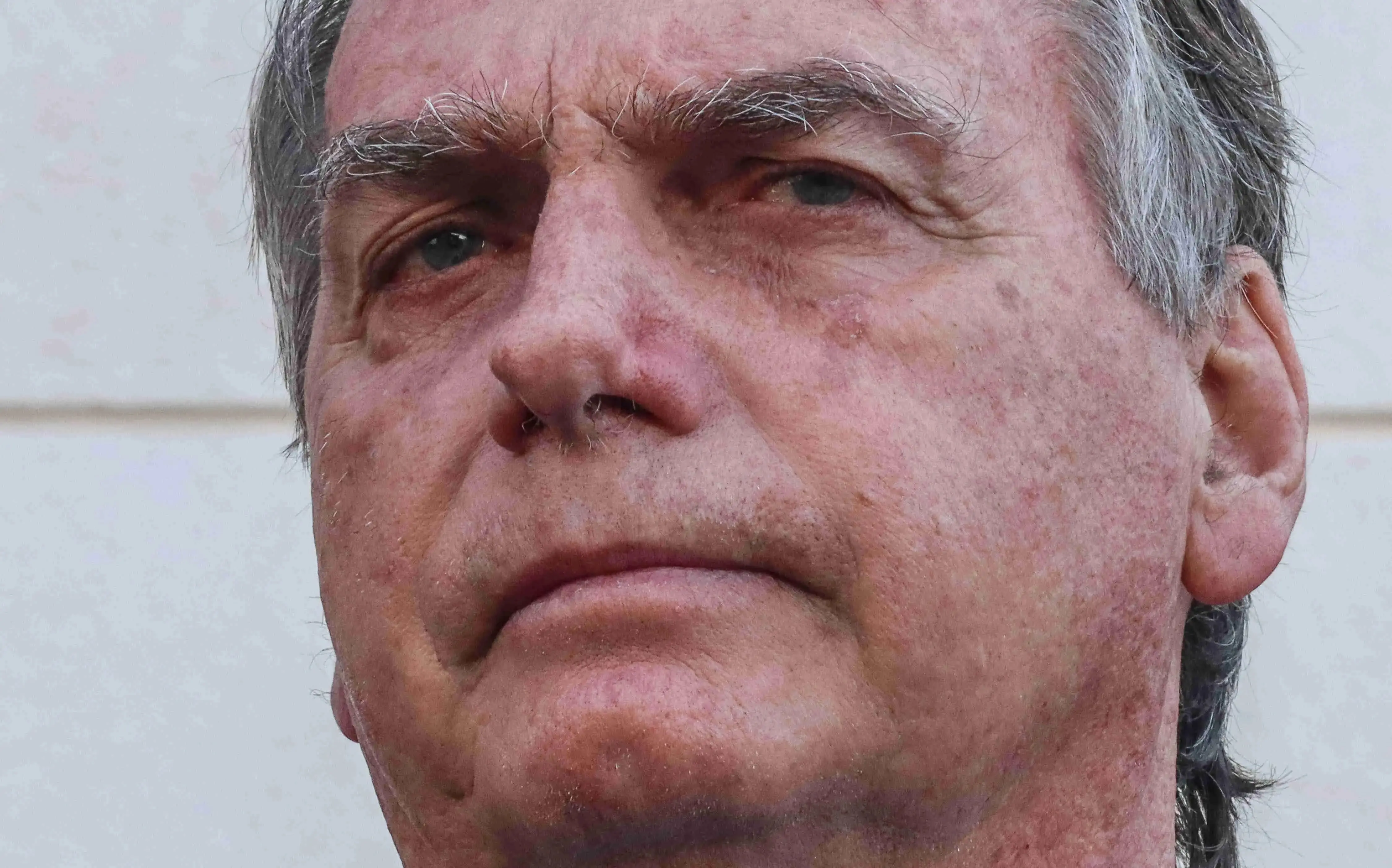 Close no rosto de Jair Bolsonaro, homem idoso, de expressão séria, pele clara com marcas e rugas visíveis, sobrancelhas grossas e cabelos grisalhos. Para matéria sobre dosimetria da pena após julgamento