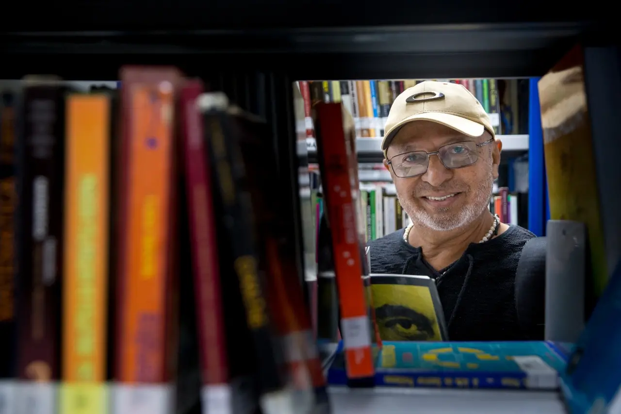 Rosto de homem aparece entre livros em estante.