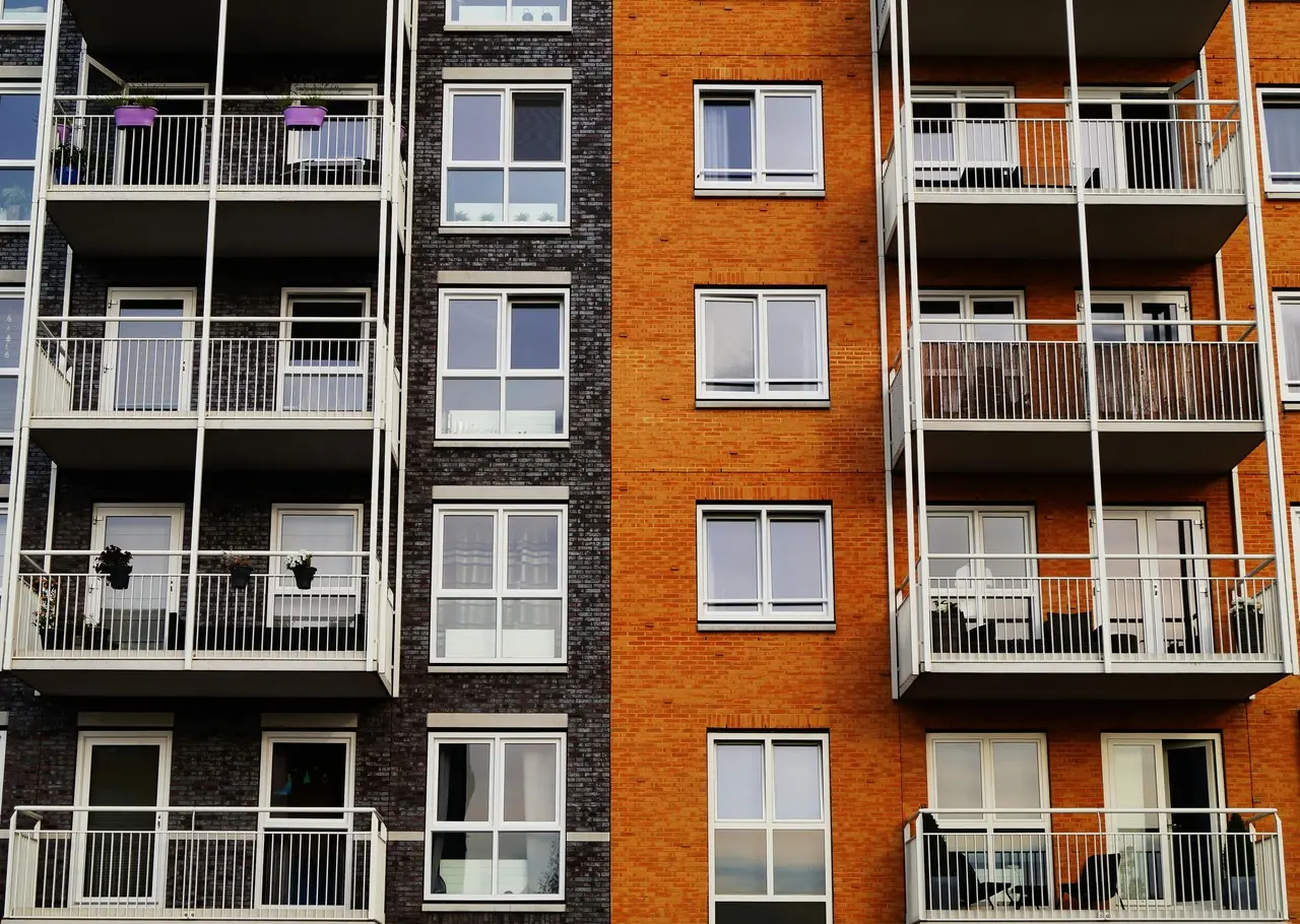 Fachada de prédio residencial com varandas, onde o lado esquerdo tem tijolos escuros e o direito tijolos alaranjados, criando contraste nas cores