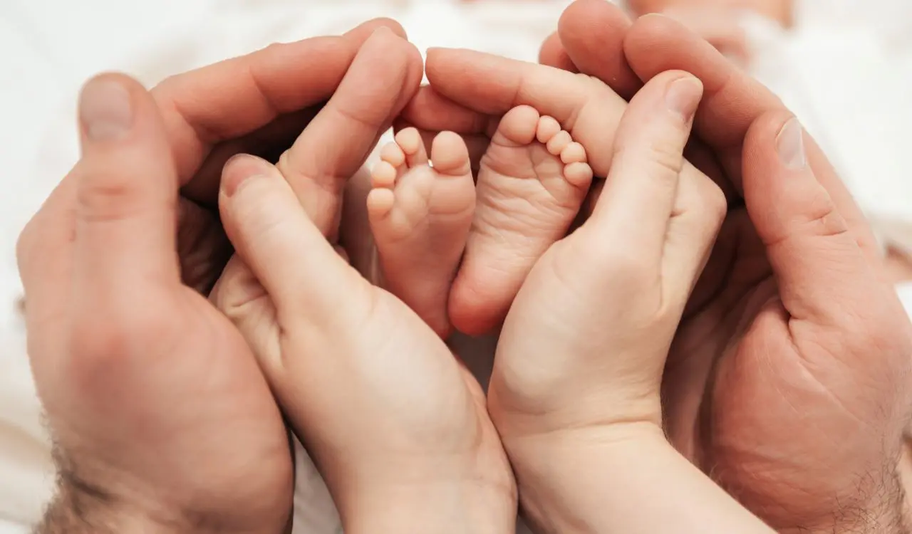 mãos seguram pés de bebê recém-nascido, em formato circular