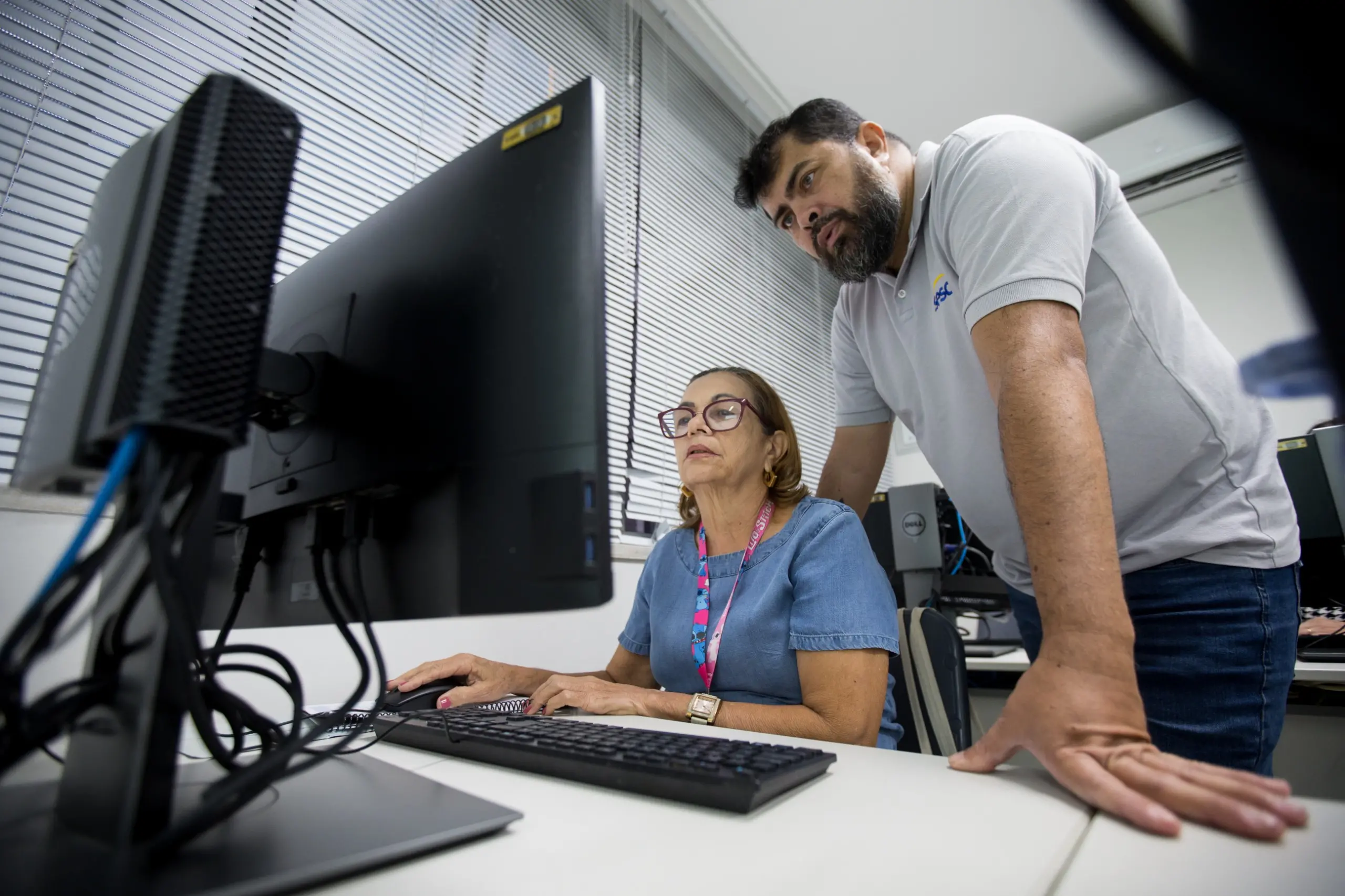 Imagem mostra idosa em frente ao computador enquanto professor ensina.