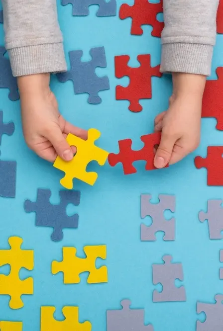 Mãos de criança brincam com quebra-cabeça nas cores que simbolizam o autismo