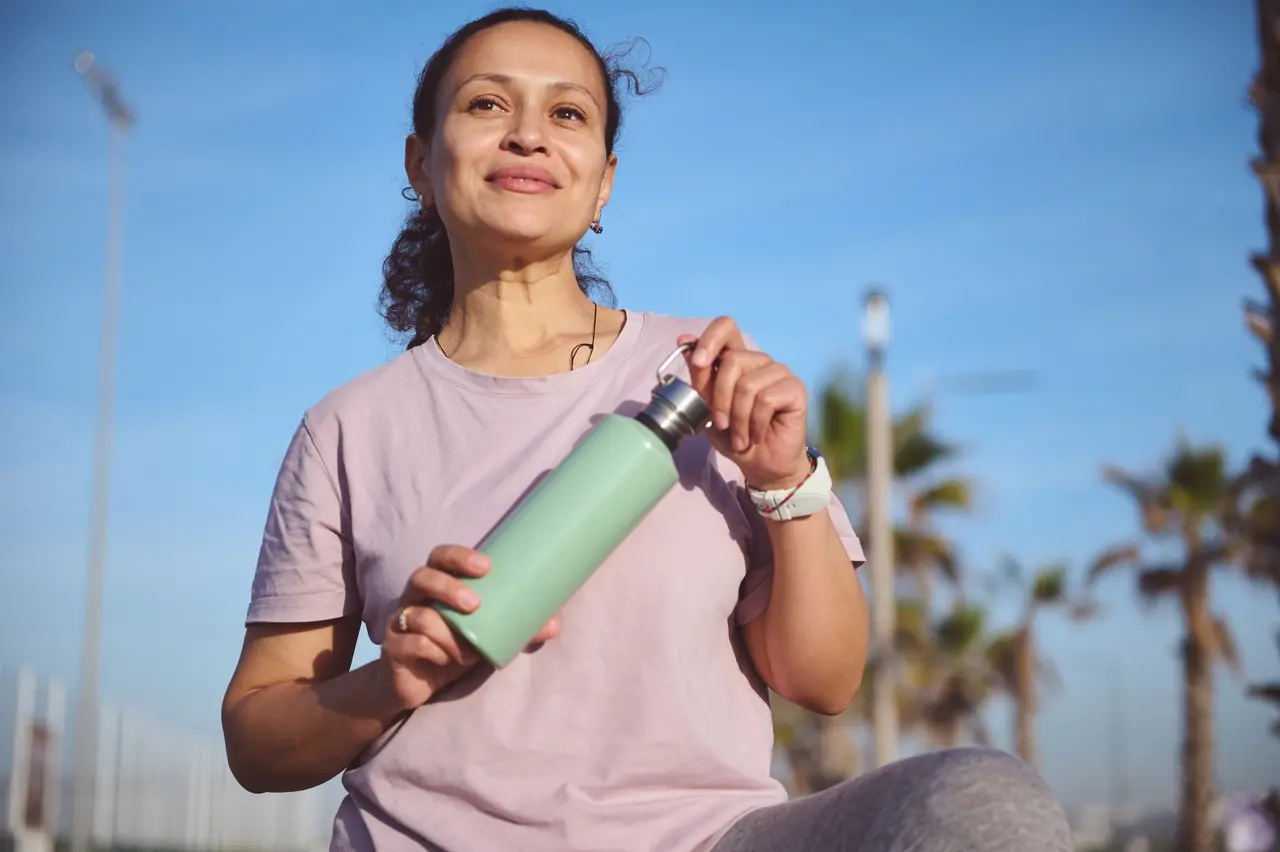 Imagem mostra mulher de meia-idade se exercitando ao ar livre e segurando garrafa de água, simbolizando bem-estar e hábitos saudáveis após os 40 anos.