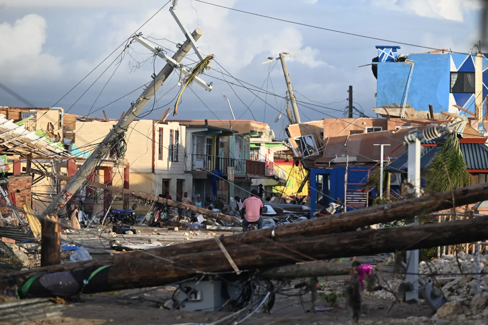Postes de energia elétrica caídos enquanto um homem pedala pela vizinhança destruída da Rua Norte, em Black River, Jamaica, em 29 de outubro de 2025, após a passagem do furacão Melissa.