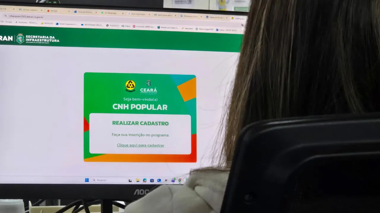 Uma pessoa, vista pelas costas e com cabelos longos, senta-se em uma cadeira em frente a um monitor de computador. A tela exibe o site do DETRAN Ceará (detran.ce.gov.br). O foco principal é a página de boas-vindas do programa 