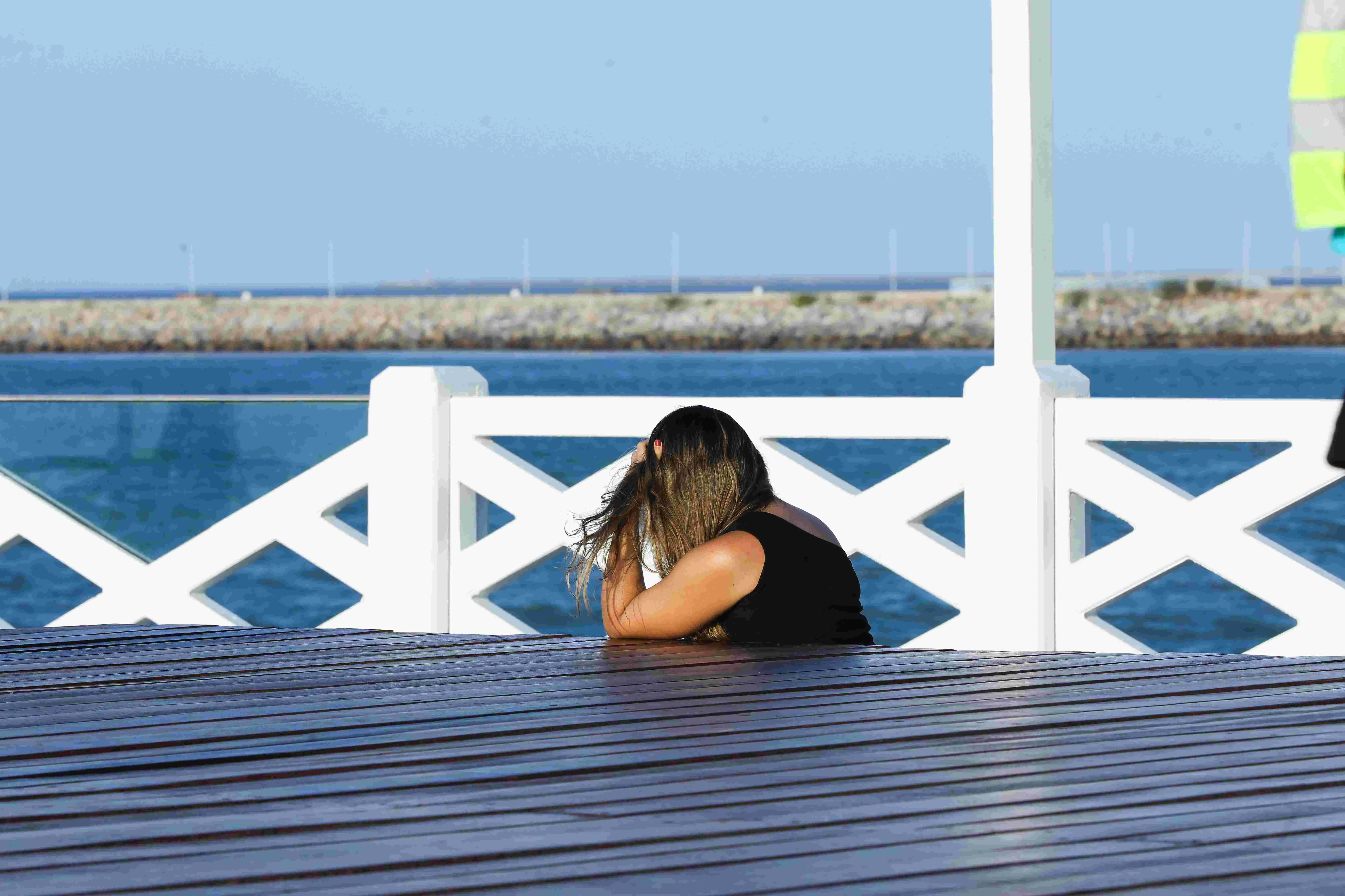 Imagem mostra mulher sentada em plataforma de madeira na Ponte dos Ingleses, em Fortaleza. Ela tem cabelos castanhos e está de costas, vestindo uma blusa preta. Diante dela, em segundo plano na foto, o mar.
